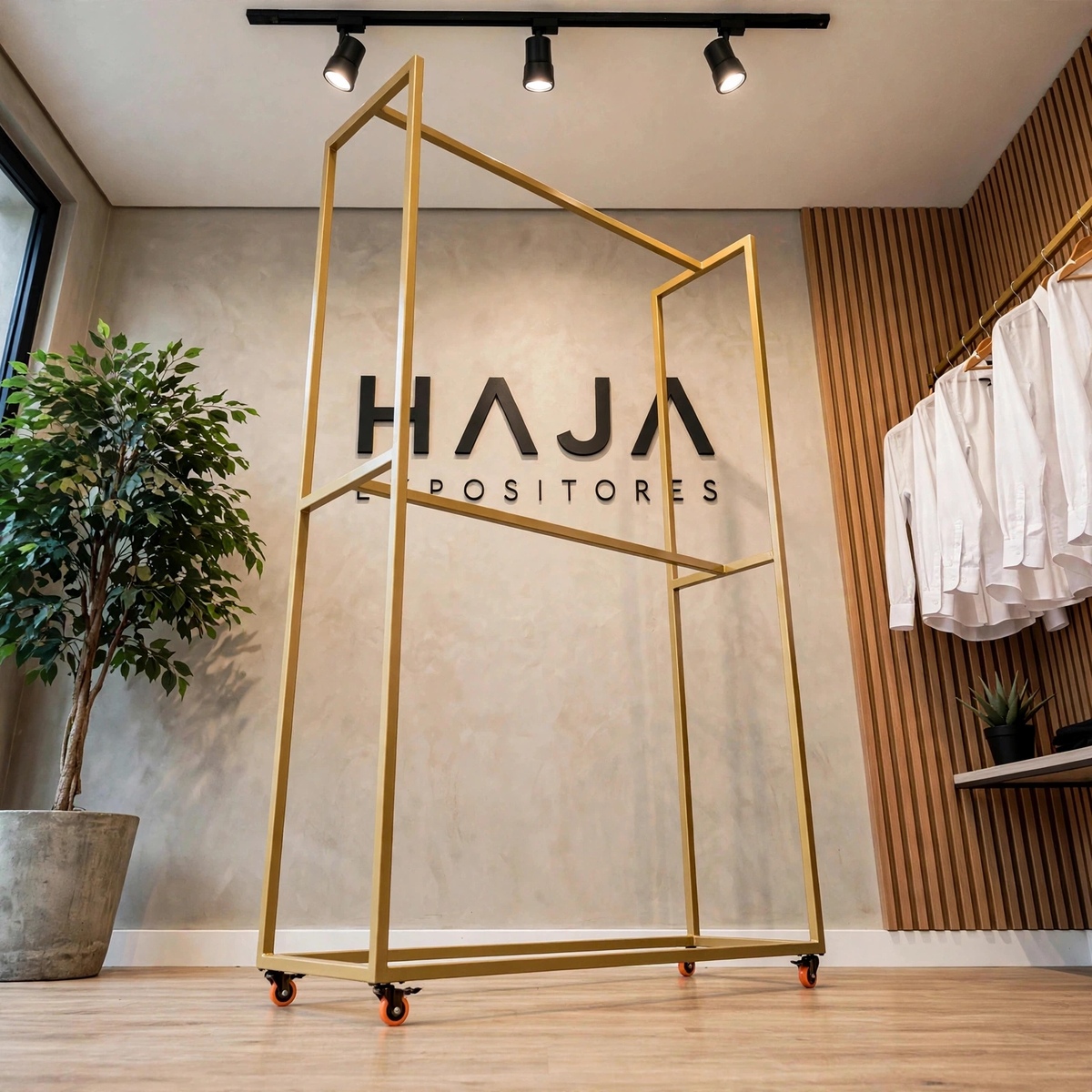 Arara Dourada de Roupa Dupla Alta com Rodas de 2.25 metros de altura por 1.5 metros de largura e 0.45 metros de profundidade, com pintura eletrostática fosca, posicionada em showroom elegante com o logotipo da HAJA Expositores ao fundo.