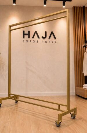 Arara Dourada de Roupa Reforçada com Rodas para peso de 2 metros de altura por 1.5 metros de largura, com pintura eletrostática fosca e rodinhas de silicone, posicionada em showroom elegante com o logotipo da HAJA Expositores ao fundo.