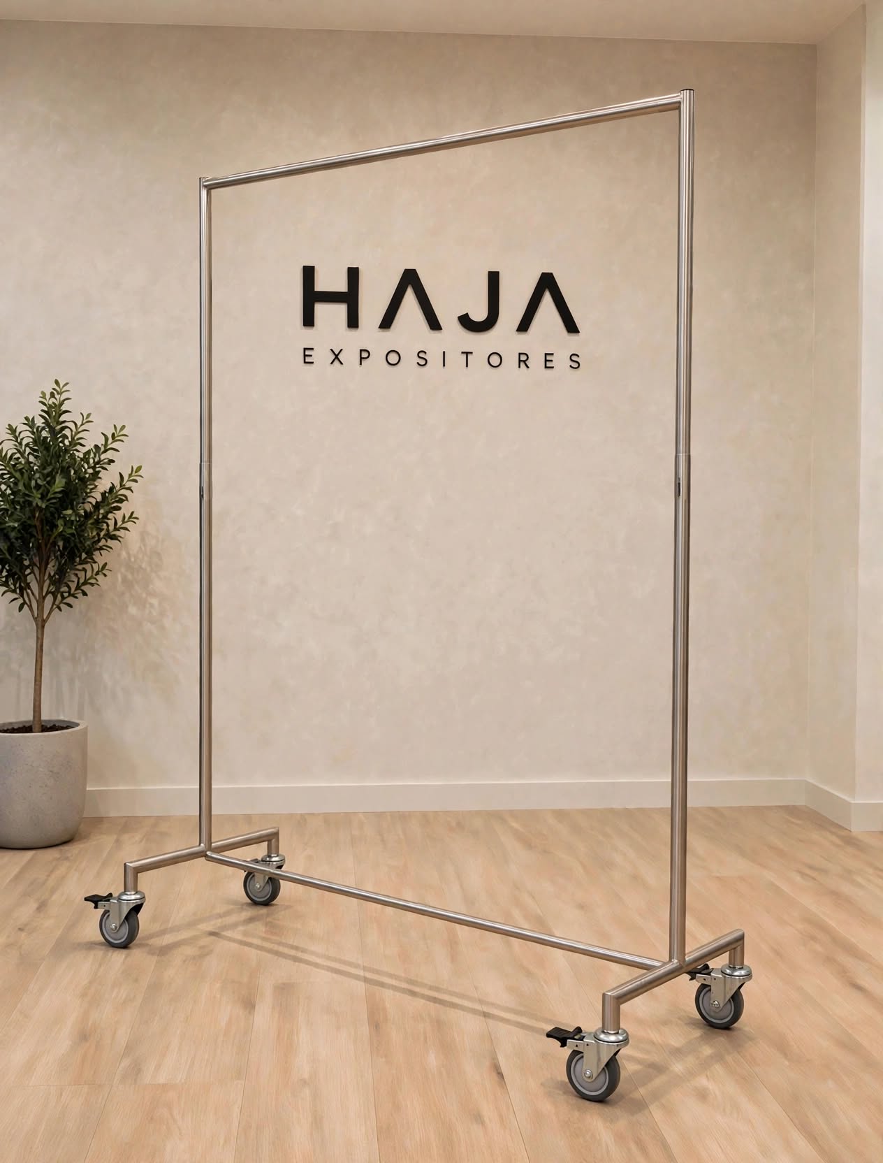 Arara Hospitalar de Inox Reforçada com Rodas de 2 metros de altura por 1.80 metros de largura em aço inoxidável AISI 304, com base larga reforçada e rodinhas de alta performance, posicionada em showroom elegante com o logotipo da HAJA Expositores ao fundo.