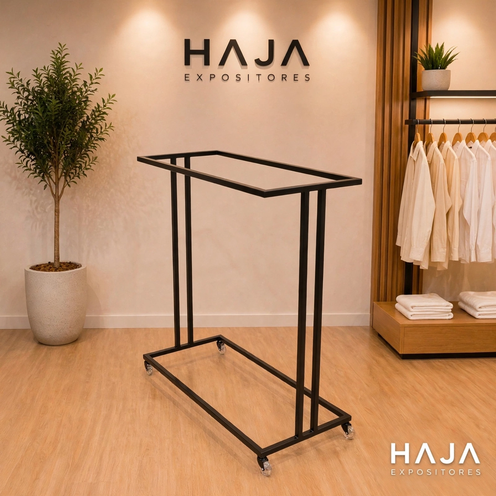 Arara Preta de Roupa Dupla com Rodas de 1.7 metros de altura por 1.5 metros de largura, com pintura eletrostática preta fosca e rodinhas de silicone, posicionada em showroom elegante com o logotipo da HAJA Expositores ao fundo.